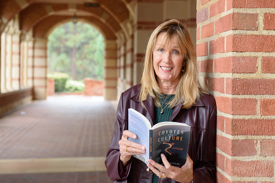 McEachern holding an opened copy of her book while leaning against brick wall.